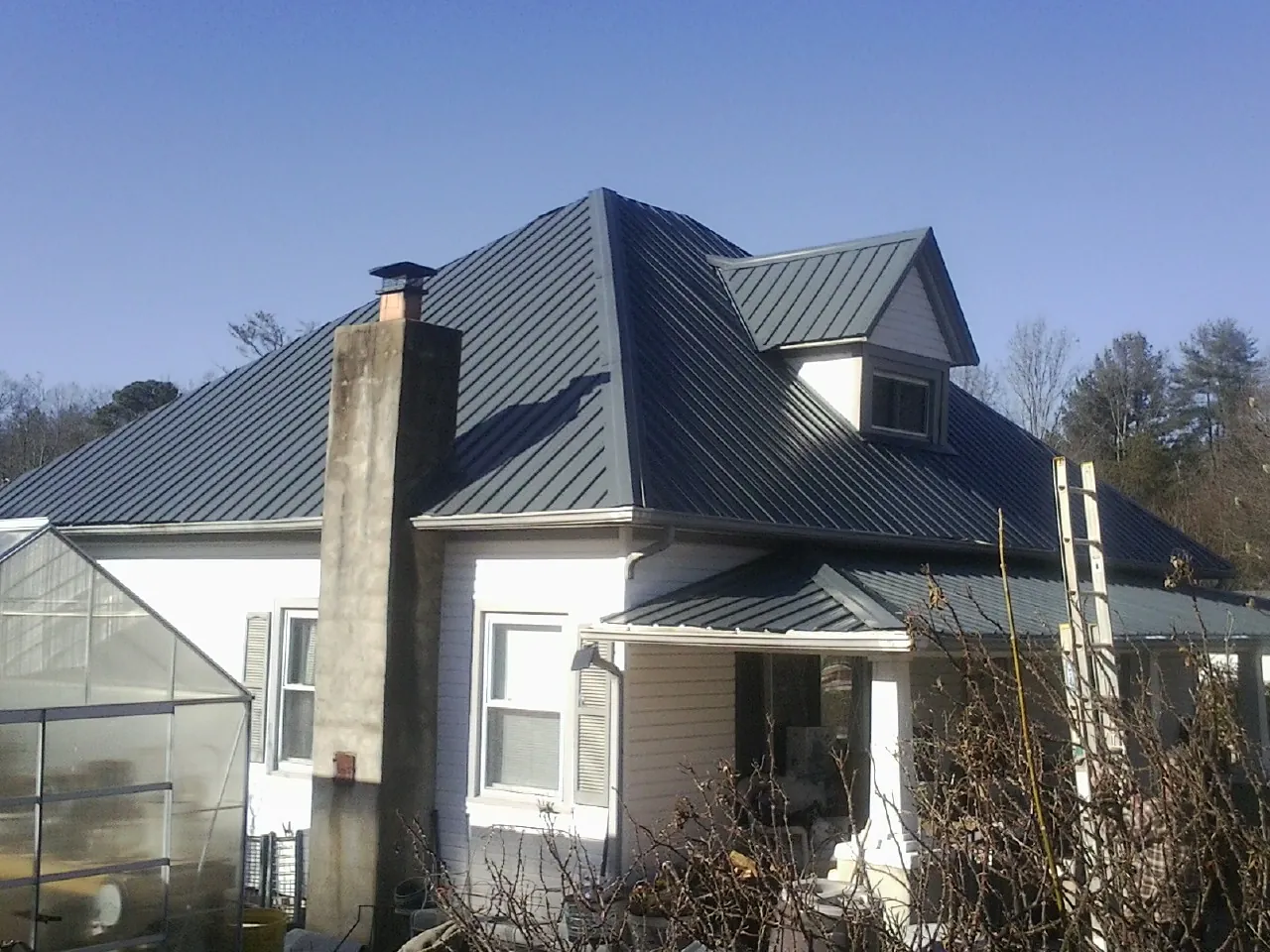 Dark blue standing seam metal roof on a white farmhouse with dormer in Mount Hope
