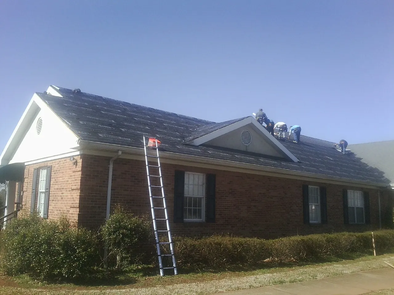 Crew tearing shingles off a brick ranch roof with a ladder set — Metal Roof Repair work by our crew in Mount Hope