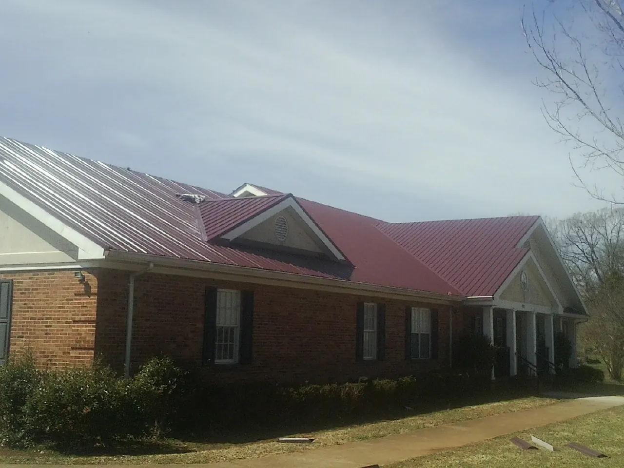 Red metal roof with gabled entries on a long brick building, from a Hail Damage Roof Repair job in Mount Hope