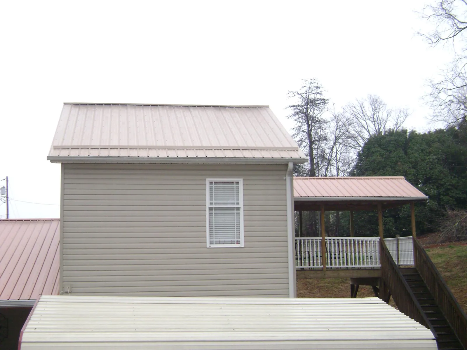 Tan metal roofs on a two story addition and attached porch, from a Roof Replacement job in Mount Hope